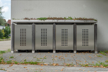 Aesthetic garbage bin with metal doors, wood and plants in front of a house wall 