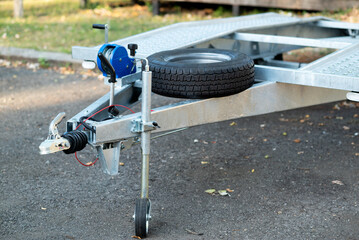 A close-up of a metal trailer hitch with a mounted spare tire and a manual winch.