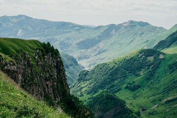 Fototapeta premium Breathtaking view of a green mountain valley with steep cliffs and rolling hills under a cloudy sky. Perfect for nature, travel, and adventure themes. High-quality, scenic landscape.