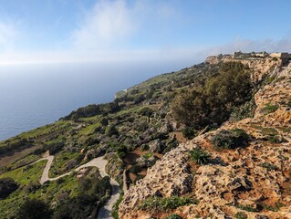 Panoramic coastal view with rocky terrain, green landscape, and expansive ocean under a clear blue sky. Perfect for nature, travel, and scenic themes. High-quality, serene vista.