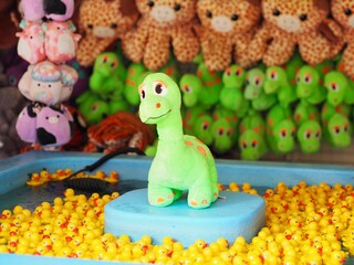 Dragon plushie toy in the amusement park with yellow ducks and lots of toys in the background. Green color stuffed dinosaur toy. © ssavelyeva1