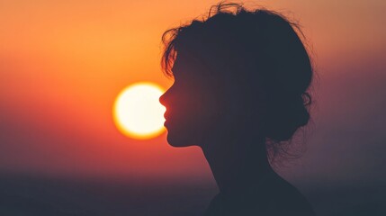 Close-up of a dramatic silhouette of a person standing against a setting sun, with warm orange and pink hues in the sky