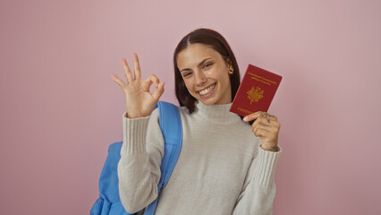 Young woman with brunette hair holding a french passport and signaling ok isolated over a pink...