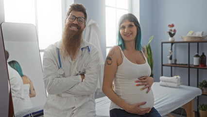 Fototapeta premium Pregnant woman standing beside male doctor in clinic room with medical equipment and smiling faces in the background, illustrating a positive prenatal care experience.