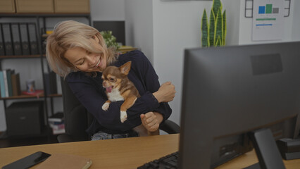 A young blonde woman is smiling while holding a chihuahua in a police station office setting,...