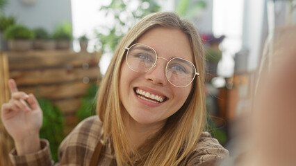 Smiling young woman with glasses taking a selfie inside a vibrant flower shop