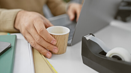 Close-up of a man's hands working in an office, with a coffee cup and laptop indicating a corporate environment.