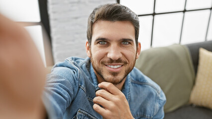 Fototapeta premium Handsome man with beard wearing denim in a cozy living room, smiling at the camera.
