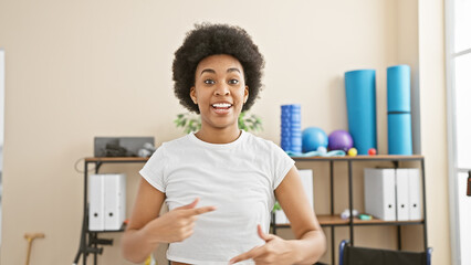 African american woman with curly hair smiling in a gym, showing exercise, wellness, and indoor...