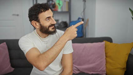 Smiling bearded man pointing in modern apartment living room.