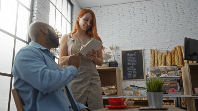 Woman waitress taking order from man customer in a bakery with shelves of bread in the background