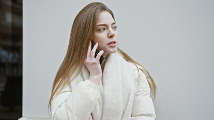 A young caucasian woman talks on the phone on a city street, showcasing an urban, outdoors setting.