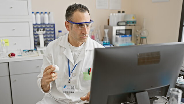Focused man in labcoat analyzing data on computer in science laboratory setting.