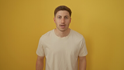 Handsome young hispanic man in a beige shirt standing isolated against a vibrant yellow background,...