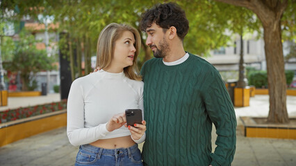 A loving couple sharing a moment outdoors, with the woman showing her smartphone to the man in a city park.