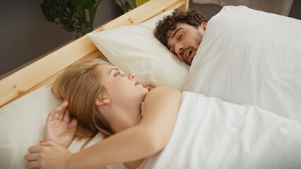 A man snoring irritates his partner in a domestic bedroom setting, highlighting relationship...