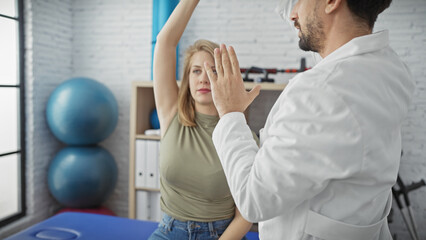 Obraz premium A woman patient exercises under the guidance of a male physiotherapist in a clinic room.