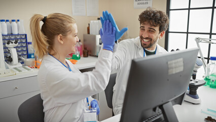 Fototapeta premium A man and woman in lab coats high-five in a bright laboratory, embodying teamwork and success in a medical or scientific environment.