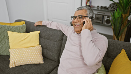 Fototapeta premium Smiling senior man using smartphone on couch in cozy living room