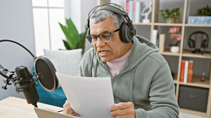 Mature man with headphones reading script in radio studio interior