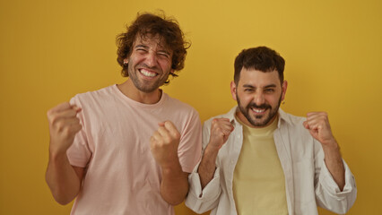 Men friends celebrating and smiling together against an isolated yellow background, showing a...