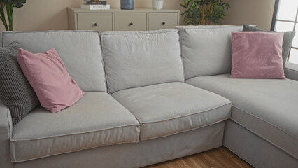 Cozy and modern living room interior featuring a grey sofa with pink throw pillows, wooden floor, indoor plants, and a cabinet with decorative items in an inviting home setting.