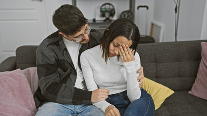 A concerned man comforts a distressed woman on a couch in a home setting, evoking themes of support and care.