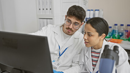 Obraz premium A man and woman in lab coats work together in a laboratory with computers and scientific equipment.