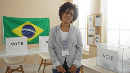Smiling african american woman standing in a brazilian electoral room with voting booths and ballot box.