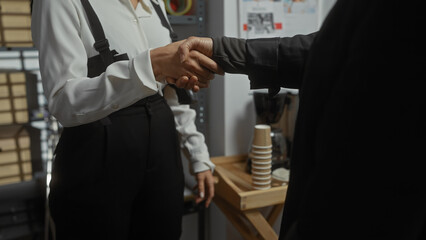 Obraz premium Two professionals in a handshake indoors, representing partnership and collaboration in a business environment.