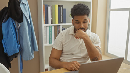 Pensive african american man working on laptop at home, reflecting modern remote work lifestyle.