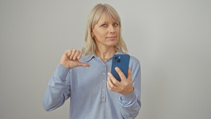 Caucasian woman holding phone showing thumb down gesture against white background