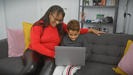 A smiling woman and boy enjoy using a laptop together on a cozy couch in a modern living room.