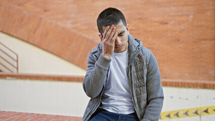 A young hispanic man appears troubled on an urban street, evoking emotions of worry or sadness in...