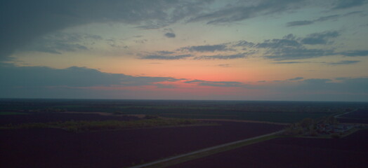Sunset over a vast, dark plowed field with a dramatic, cloudy sky.