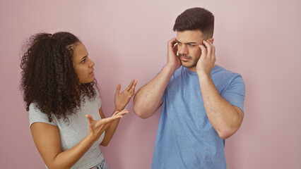 A frustrated woman argues with a displeased man covering his ears against a pink background.