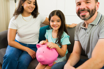Family happily teaches their daughter the value of saving money while lounging on the sofa in their...