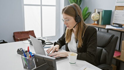 A professional woman in an office setting wearing a headset and using a laptop for business communication