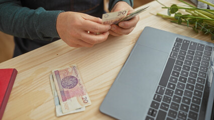 A young man counts polish currency in a flower shop with a laptop and bouquet nearby, indicating a...