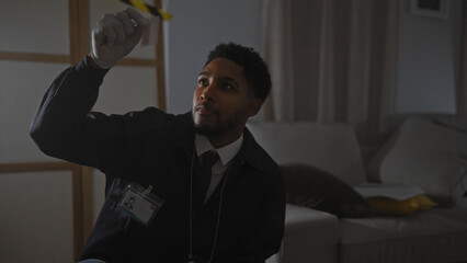 A focused african american man examines evidence at a dimly-lit indoor crime scene.