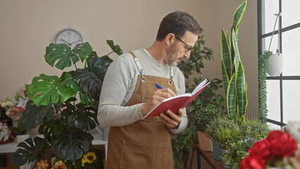 Bearded man in apron writing inventory at lush flower shop