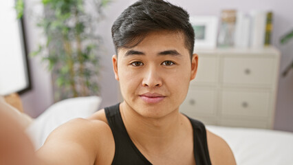 Handsome young asian man taking selfie in cozy bedroom interior
