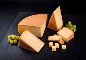 Traditional aged mountain cheese of the Alps offered as close-up with grapes on a design board