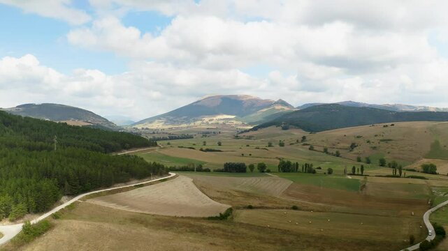 Aerial view of the wild Colfiorito Plateau in Central Italy, nestled in the Apennines between Umbria and Marche. The landscape is mostly untouched, with farmland and a few small roads