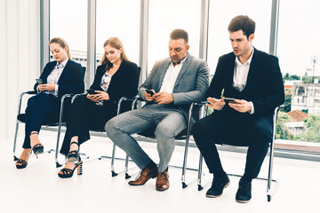 Businesswomen and businessmen using mobile phone while waiting on chairs in office for job interview. Corporate business and human resources concept. uds