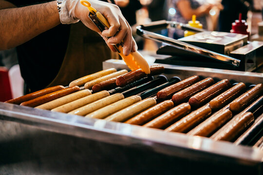 A vendor fries sausages at a hot dog stand.