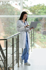 Smiling nurse with laptop near railings in hospital