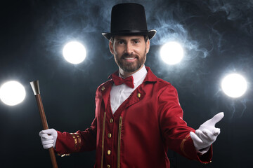 Portrait of showman in red costume, cane and hat on black background with spotlights and smoke