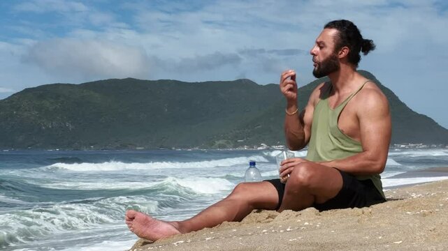 Man on a sunny day at the beach having a picnic, eating and drinking water. Outdoor concept.