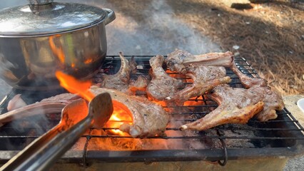 Grilled French lamb cutlets. Lamb chops on the grill with flames and a small pot of marinade. BBQ concept Close Up. Wire rack for roast lamb on the grill